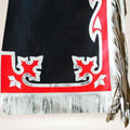Black blanket with red and white patterns and fringes on a beige background