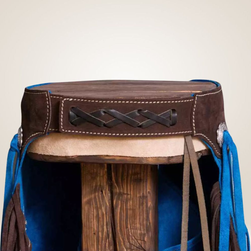 Blue and brown leather saddle blanket with fringes on a stand against a beige background
