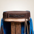 Close-up of a brown leather saddle with blue straps on a wooden stand.