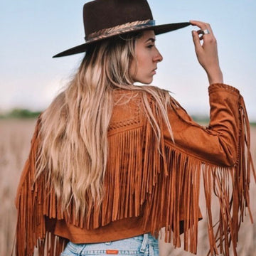 Woman wearing a brown fringed jacket and hat in an outdoor setting