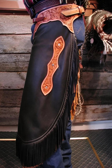 Decorative leather chaps with fringe and intricate designs on a wooden background